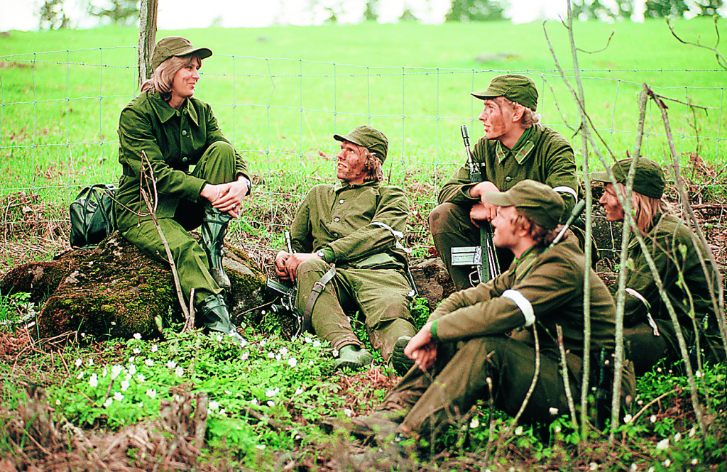 Fikapaus i gröngräset, en kvinnlig personalassistent samtalar med värnpliktiga soldater. Året är 1976. Foto: TT Nyhetsbyrån